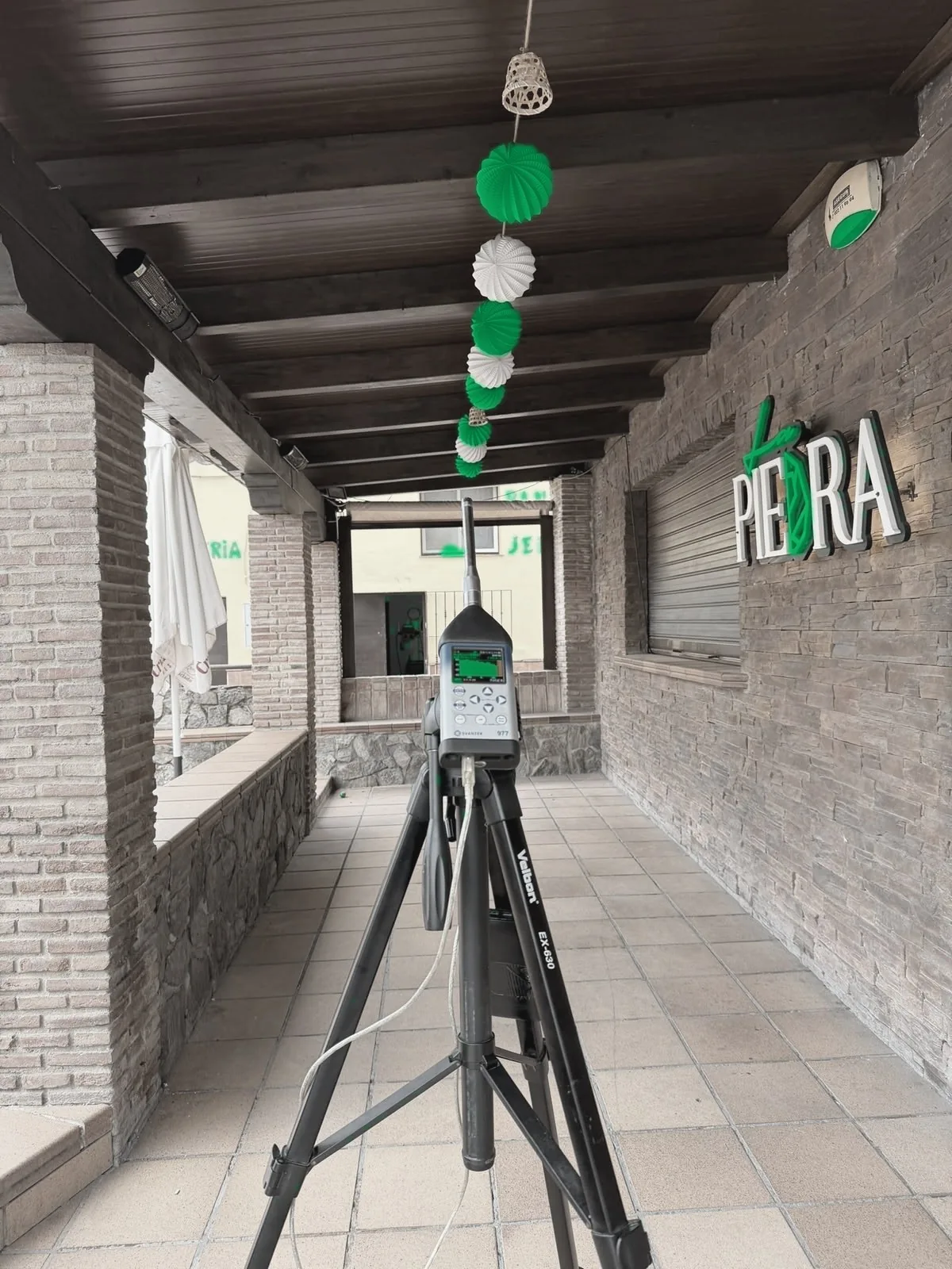 Sonómetro profesional instalado en un espacio de actividad con elementos verdes de la marca